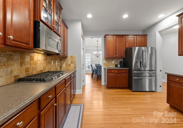 kitchen featuring pendant lighting, appliances with stainless steel finishes, tasteful backsplash, light hardwood / wood-style floors, and an inviting chandelier