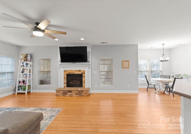 living room featuring a stone fireplace, light hardwood / wood-style flooring, and ceiling fan with notable chandelier