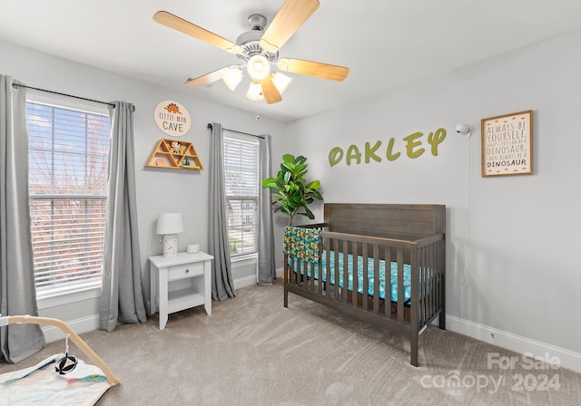 carpeted bedroom with a crib, multiple windows, and ceiling fan