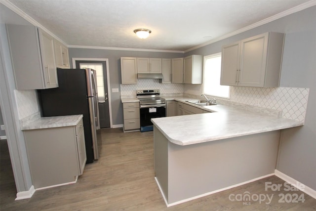 kitchen with ornamental molding, backsplash, appliances with stainless steel finishes, light wood-type flooring, and kitchen peninsula