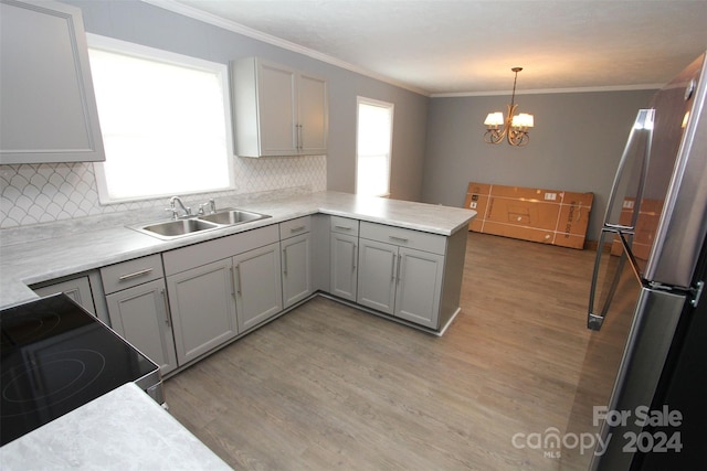 kitchen with sink, kitchen peninsula, pendant lighting, stainless steel fridge, and light wood-type flooring