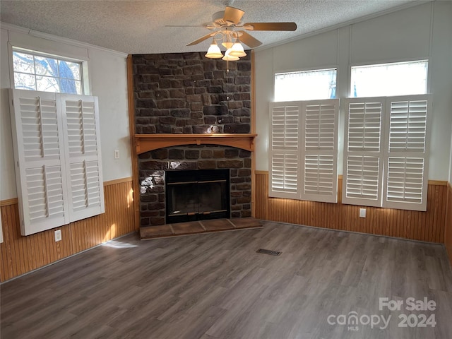 unfurnished living room with hardwood / wood-style floors, a stone fireplace, ornamental molding, and a textured ceiling