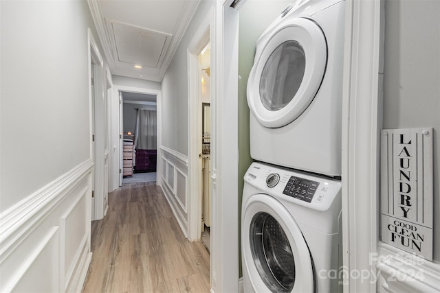 clothes washing area featuring stacked washer / dryer, crown molding, and light hardwood / wood-style flooring