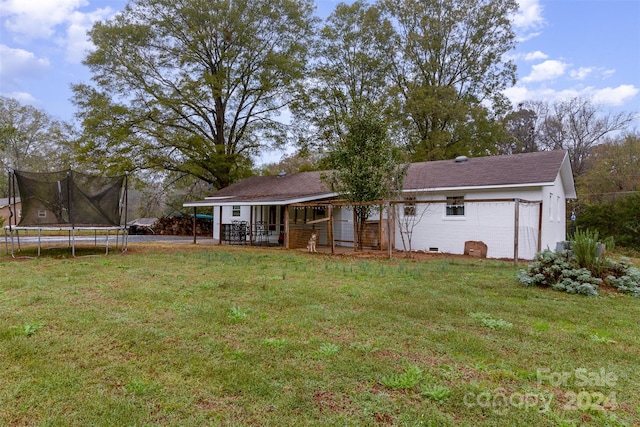 rear view of property featuring a trampoline and a yard