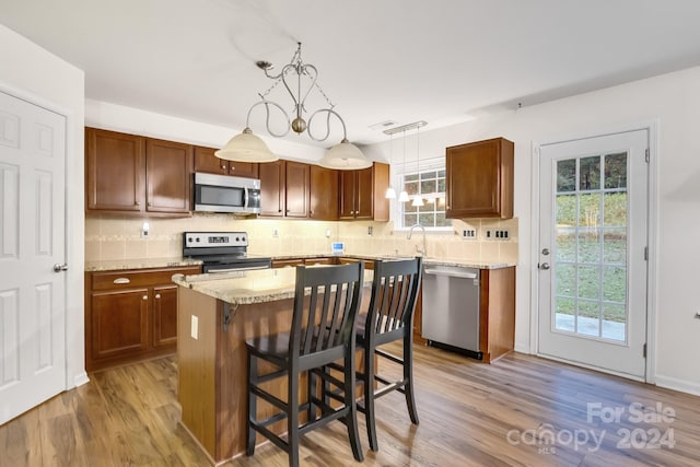 kitchen featuring appliances with stainless steel finishes, decorative light fixtures, a kitchen island, and light hardwood / wood-style flooring