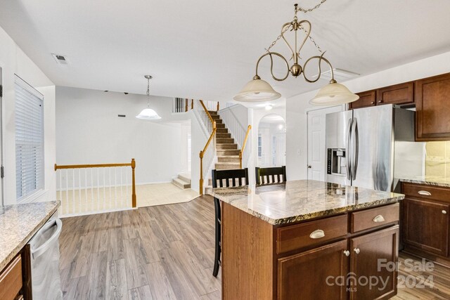 kitchen with light stone counters, a center island, light hardwood / wood-style flooring, pendant lighting, and appliances with stainless steel finishes