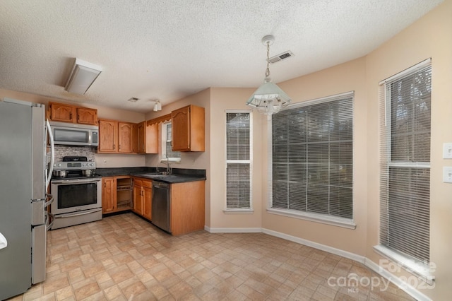 kitchen with stainless steel appliances, decorative light fixtures, sink, and a textured ceiling