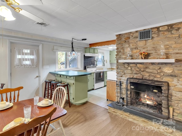 dining area featuring ceiling fan, light hardwood / wood-style floors, and a stone fireplace