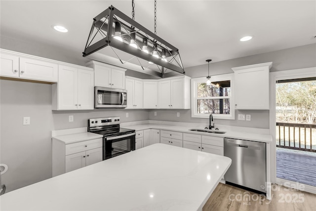 kitchen with white cabinets, stainless steel appliances, sink, and decorative light fixtures