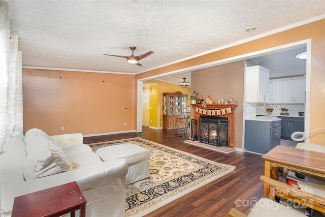 living room featuring dark wood-type flooring, ornamental molding, a textured ceiling, and ceiling fan