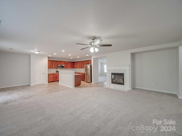 unfurnished living room with ceiling fan, a fireplace, light colored carpet, and a textured ceiling