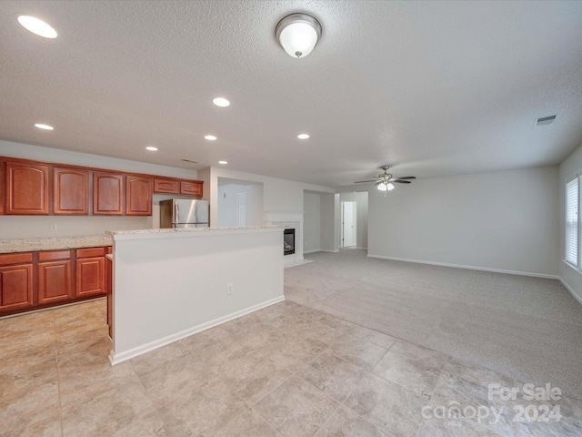 kitchen featuring ceiling fan, a textured ceiling, a kitchen island, light colored carpet, and stainless steel refrigerator