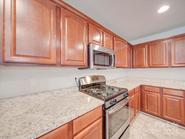 kitchen featuring a textured ceiling, light stone counters, and stainless steel appliances