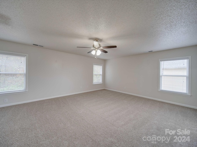 carpeted empty room with ceiling fan, a textured ceiling, and a wealth of natural light