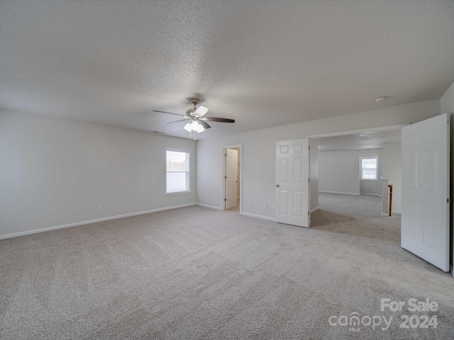 empty room with ceiling fan, light colored carpet, and a textured ceiling