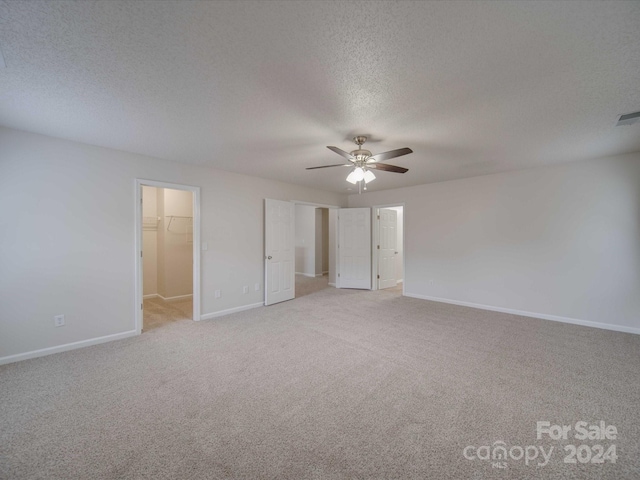 unfurnished bedroom with ceiling fan, a textured ceiling, a walk in closet, light carpet, and a closet