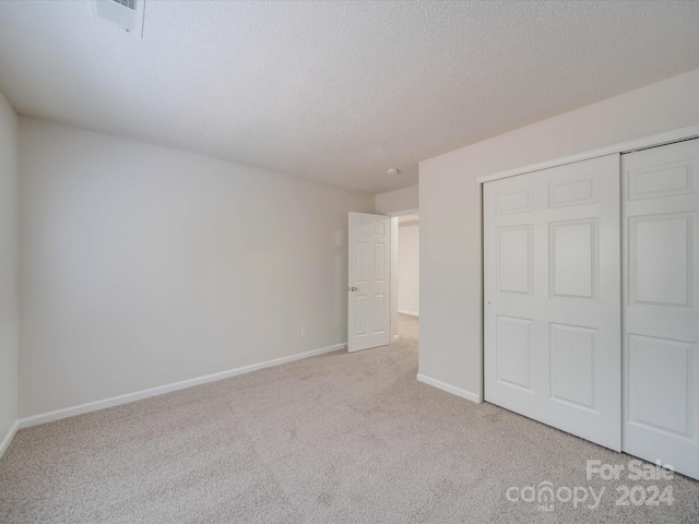 unfurnished bedroom featuring a textured ceiling, light carpet, and a closet