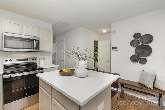 kitchen featuring light hardwood / wood-style floors, white cabinetry, appliances with stainless steel finishes, a center island, and decorative backsplash