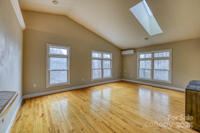 unfurnished living room with a textured ceiling, light hardwood / wood-style flooring, an AC wall unit, and vaulted ceiling with skylight