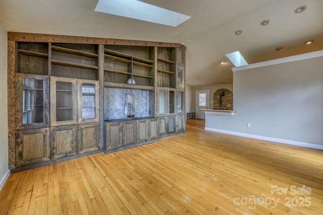 unfurnished living room featuring vaulted ceiling with skylight, hardwood / wood-style floors, and built in shelves