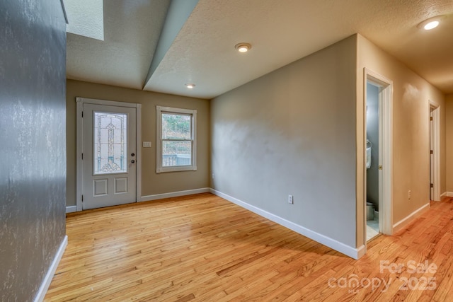 foyer entrance with light hardwood / wood-style floors, a textured ceiling, and a skylight