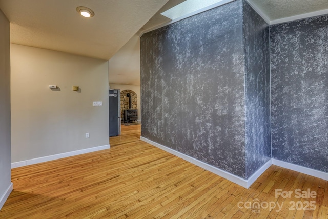 spare room featuring crown molding, a wood stove, and hardwood / wood-style flooring