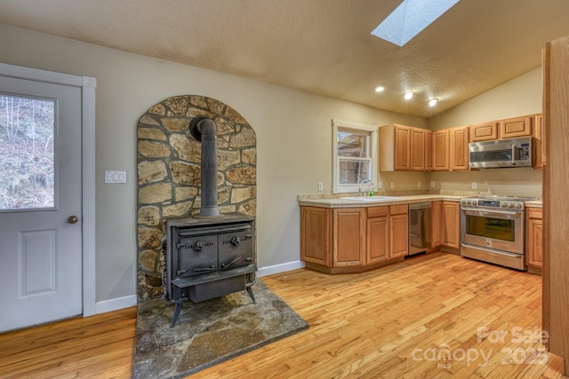 kitchen featuring light hardwood / wood-style floors, vaulted ceiling with skylight, appliances with stainless steel finishes, and sink