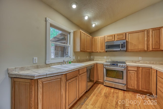 kitchen with tile countertops, stainless steel appliances, light wood-type flooring, vaulted ceiling, and sink