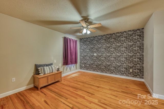 unfurnished room with a textured ceiling, ceiling fan, brick wall, and light hardwood / wood-style flooring