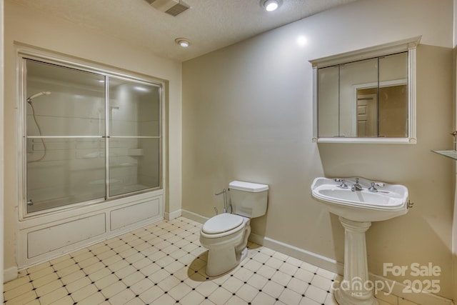 bathroom with toilet, bath / shower combo with glass door, and a textured ceiling