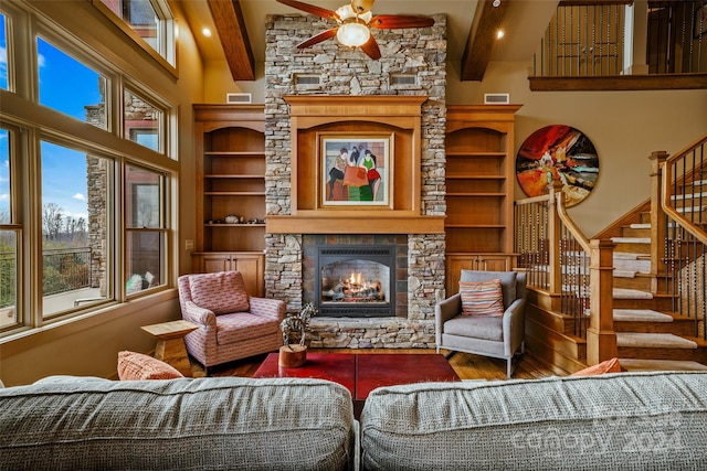 living room featuring beam ceiling, a stone fireplace, ceiling fan, and hardwood / wood-style floors