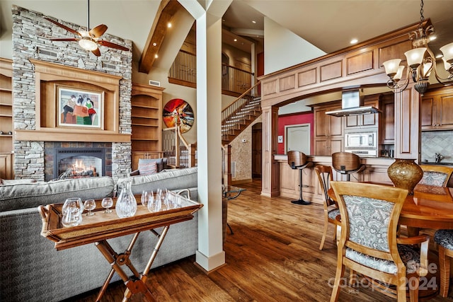 dining room with ceiling fan, dark hardwood / wood-style flooring, beamed ceiling, a towering ceiling, and a fireplace