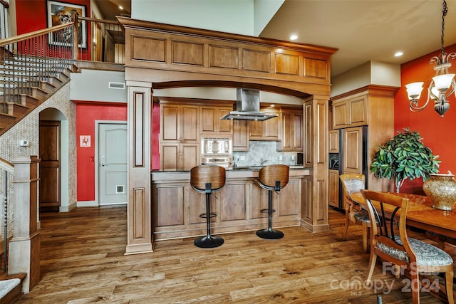 kitchen featuring backsplash, extractor fan, decorative light fixtures, hardwood / wood-style floors, and stainless steel microwave