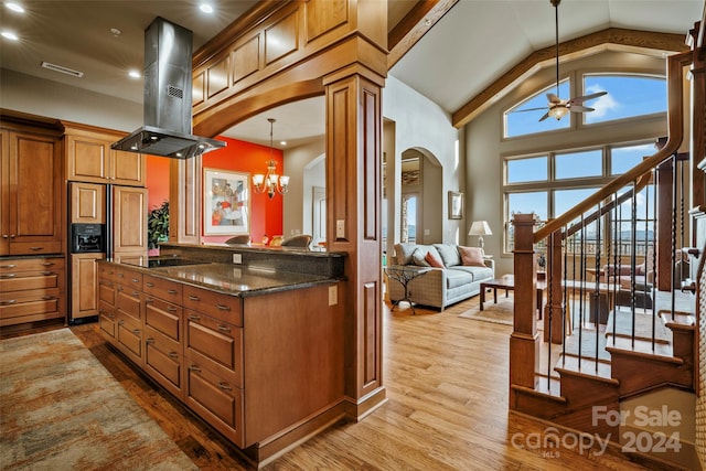 kitchen with high vaulted ceiling, island exhaust hood, dark stone countertops, pendant lighting, and light wood-type flooring