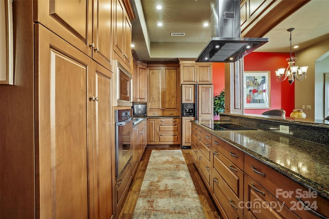 kitchen featuring hanging light fixtures, island exhaust hood, dark stone countertops, wood-type flooring, and black appliances