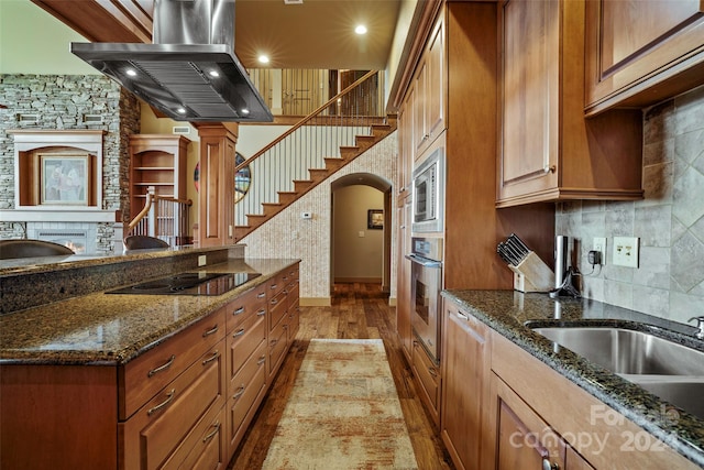 kitchen with dark stone countertops, appliances with stainless steel finishes, extractor fan, and light wood-type flooring