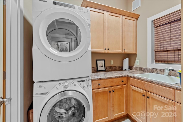 laundry room with cabinets, stacked washing maching and dryer, and sink