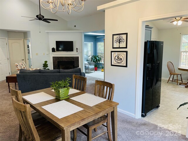 dining space featuring ceiling fan with notable chandelier, a wealth of natural light, lofted ceiling, and light carpet