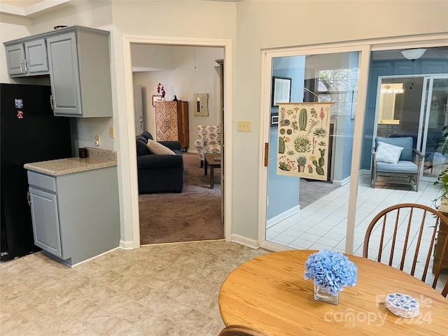 kitchen with gray cabinets, black refrigerator, and light colored carpet