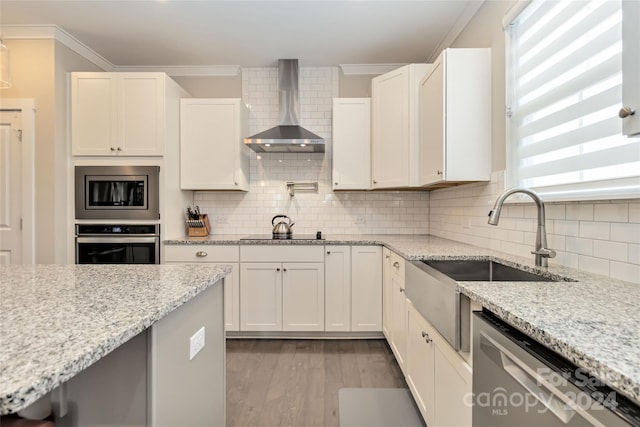 kitchen featuring stainless steel appliances, white cabinets, wall chimney exhaust hood, tasteful backsplash, and ornamental molding