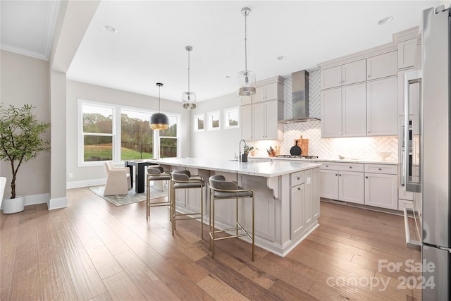 kitchen with decorative light fixtures, wood-type flooring, wall chimney exhaust hood, and a center island with sink