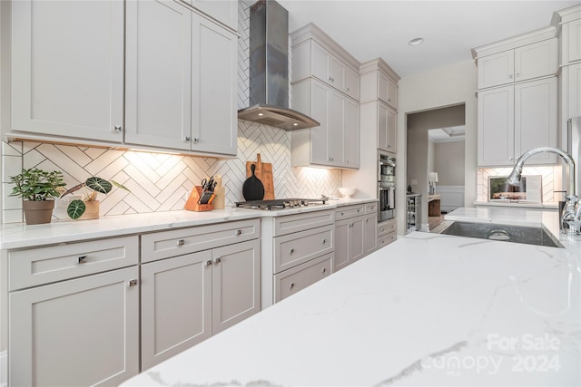 kitchen featuring tasteful backsplash, wall chimney range hood, appliances with stainless steel finishes, light stone countertops, and sink