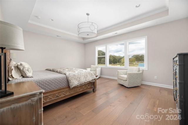 bedroom with crown molding, hardwood / wood-style floors, and a raised ceiling