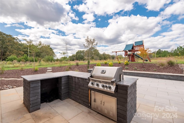 view of patio / terrace featuring a playground, an outdoor kitchen, and a grill