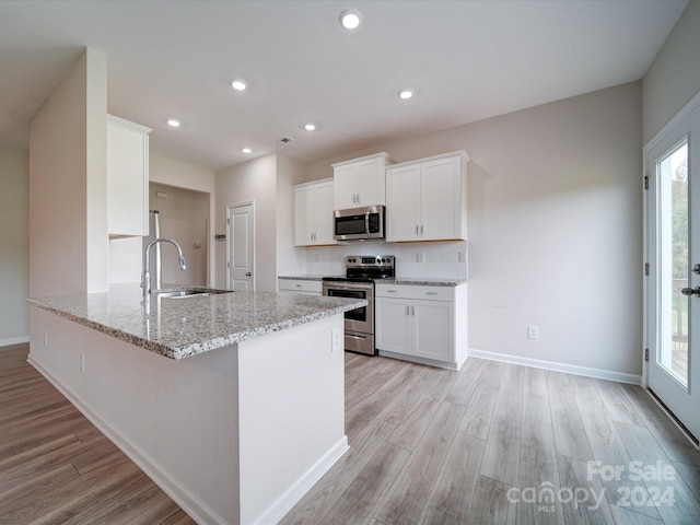 kitchen with light wood-type flooring, light stone countertops, white cabinets, and stainless steel appliances