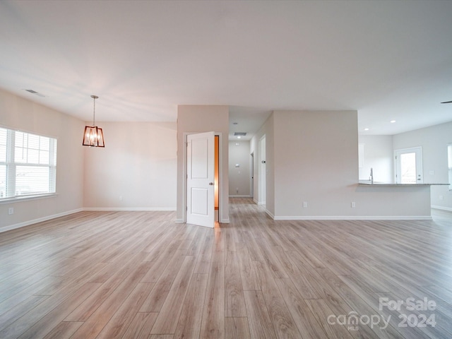 unfurnished living room with an inviting chandelier and light wood-type flooring