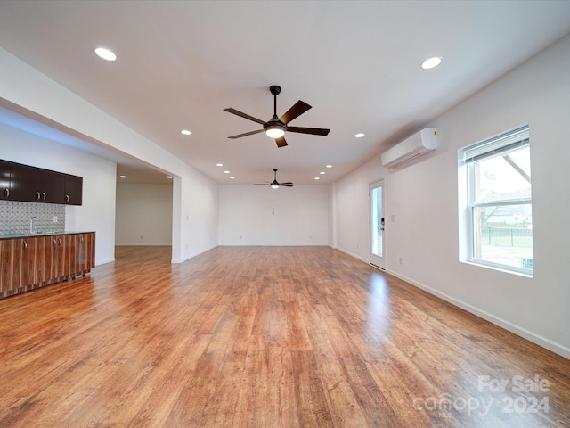 unfurnished living room with light hardwood / wood-style floors, an AC wall unit, and ceiling fan