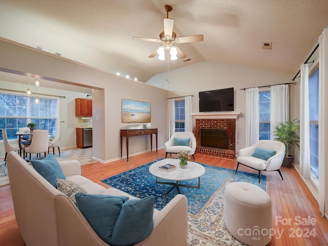 living room with a fireplace, light hardwood / wood-style flooring, a wealth of natural light, and vaulted ceiling