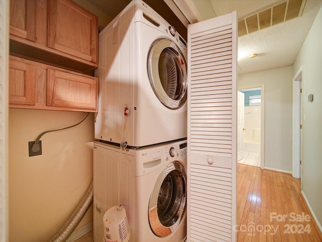 clothes washing area with stacked washer / dryer, light hardwood / wood-style floors, and a textured ceiling