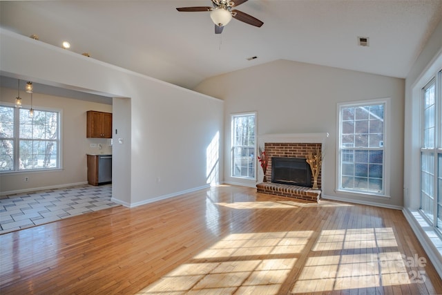 unfurnished living room featuring visible vents, light wood finished floors, lofted ceiling, plenty of natural light, and a fireplace